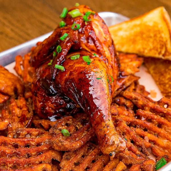 Gettin' Basted's BBQ chicken leg and thigh, garnished with scallions, served over waffle fries and toast.