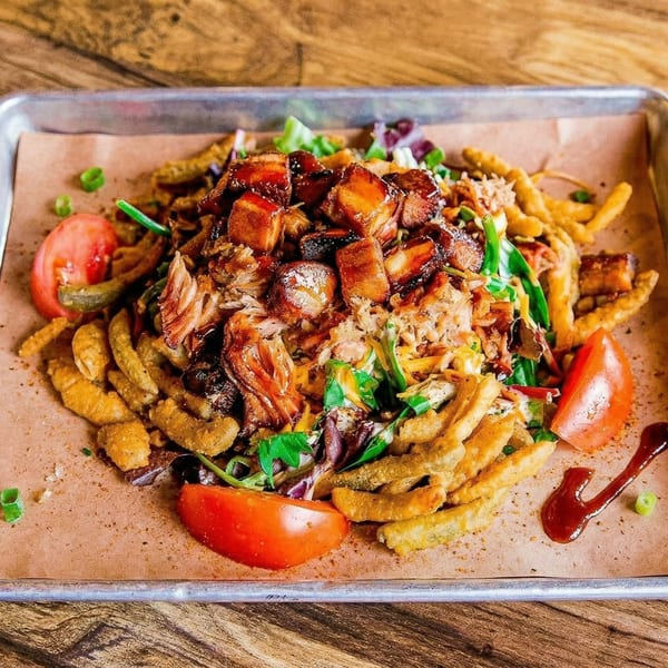 A metal tray with paper holds a dish of fried okra, pulled pork, pork belly, and tomatoes.